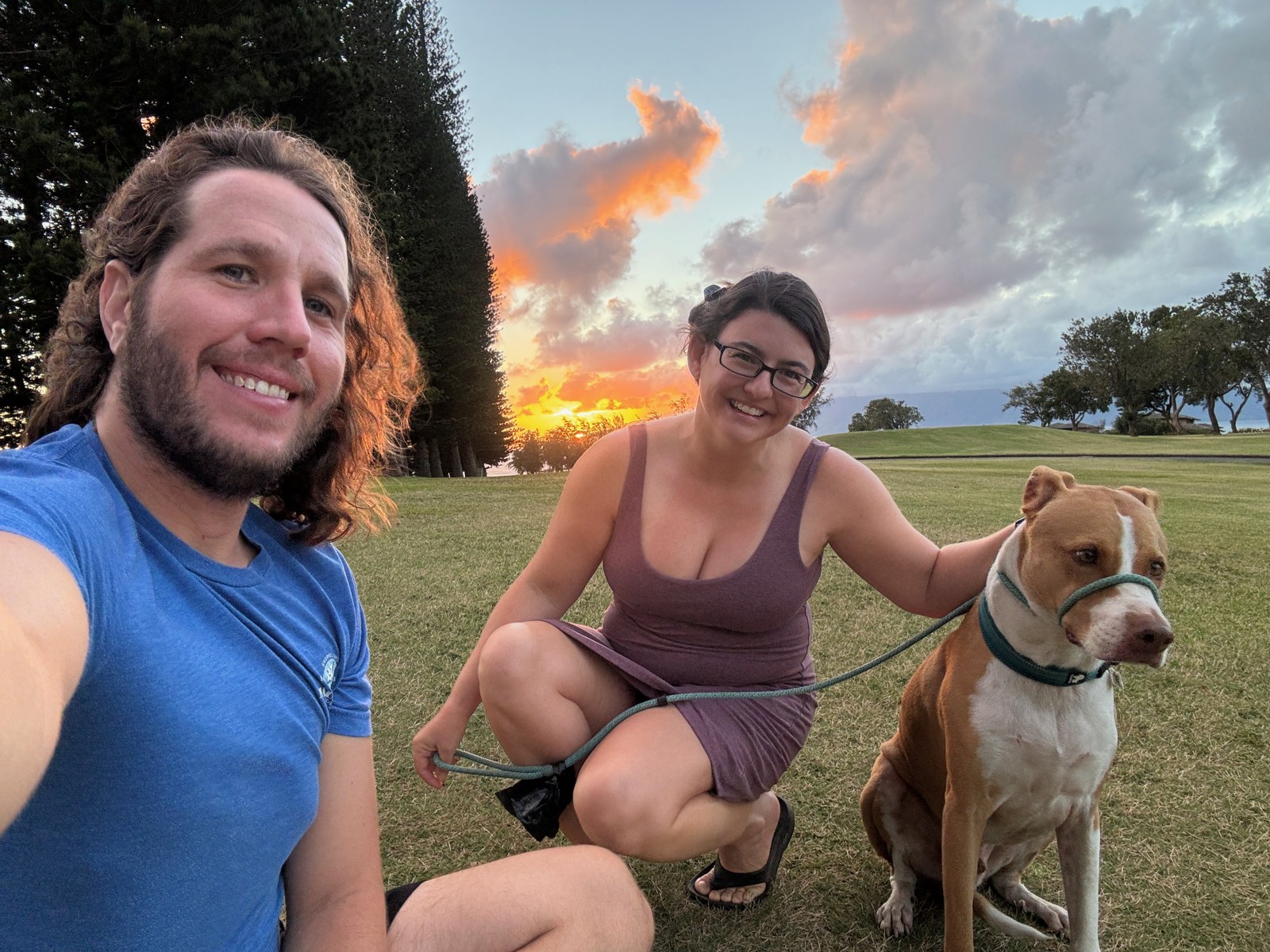 Kevin and Ashley smiling on the fairway at sunset, with Finley sitting between them.